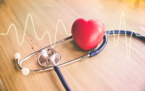 Czerwone serce i stetoskop na drewnianym tle z linią EKG.