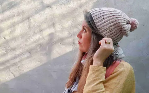 Mujer con gorro tejido a crochet, con pompón rosa. Disfruta del proceso de tejer gorros crochet.