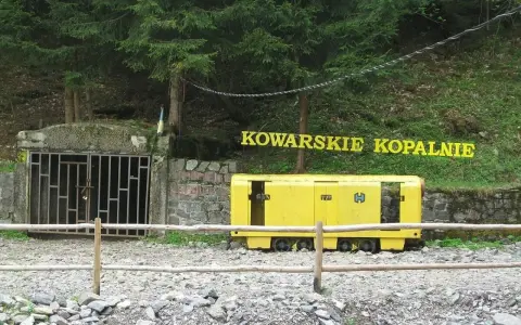 Wejście do sztolni Kowary z żółtym wagonikiem górniczym i napisem "KOWARSKIE KOPALNIE".