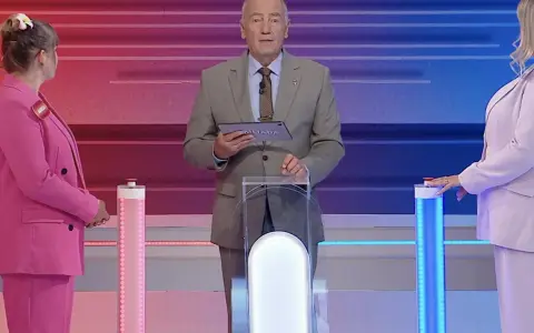 Prowadzący Familiady z tabliczką "Miliada" i dwie uczestniczki w różowych strojach. Zastanawiają się, co zmieniamy podczas jazdy samochodem.