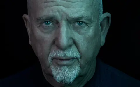 Närbild på Peter Gabriel med blå ögon och vitt skägg, ljuset ger en mystisk känsla som passar hans nya album.