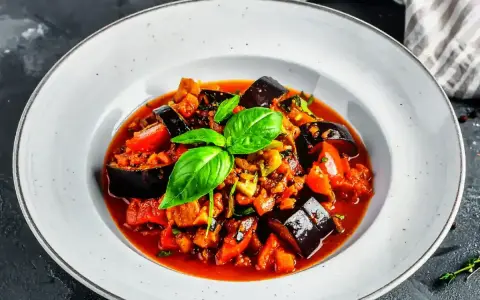 Un plat de ratatouille recette coloré et appétissant, garni de basilic frais, dans une assiette blanche.