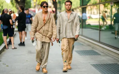 Dos hombres pasean con estilo. Uno lleva un kimono beige y pantalones de lino a rayas. El otro, una camisa a rayas y pantalones beige. Un ejemplo de cómo combinar pantalón lino beige hombre.