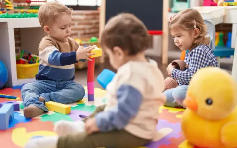 Trójka małych dzieci bawi się klockami i zabawkami na kolorowej macie w żłobku.