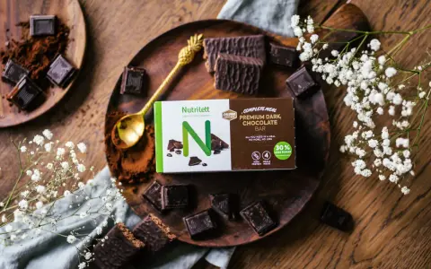 Chokladbitar och en förpackning med Nutrilett Premium Dark Chocolate Bar, en del av deras kalorisnål mat-sortiment.