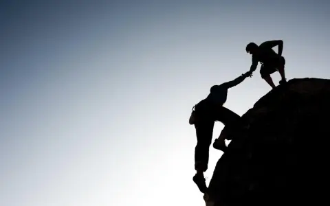 Silhouette d'un grimpeur aidant un autre à atteindre le sommet. Une belle présentation photographe de l'entraide et de la persévérance.