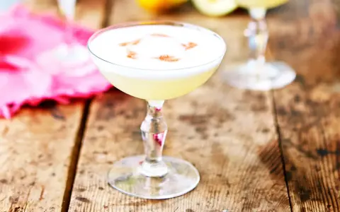 En krämig pisco sour med ett vitt skum och en touch av kanel på en rustik träyta.