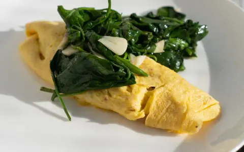 Złożony omlet francuski z zielonym szpinakiem i czosnkiem na białym talerzu.
