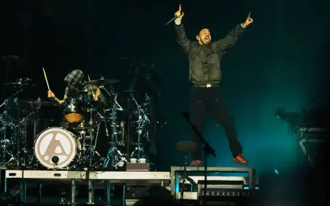 Linkin Park-Bandmitglieder auf der Bühne, ein Sänger springt, ein Schlagzeuger spielt.