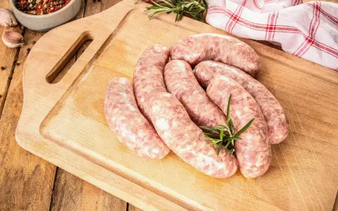 Surowe kiełbaski na desce, obok gałązka rozmarynu. Zastanawiasz się, jak długo można mrozić kiełbasę, by zachowała świeżość?