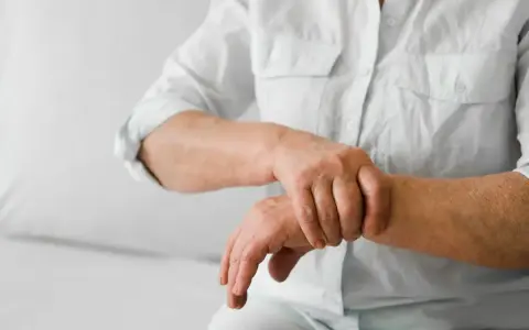 Osoba w białej koszuli masuje nadgarstek, odczuwając ból stawów rąk i nóg.
