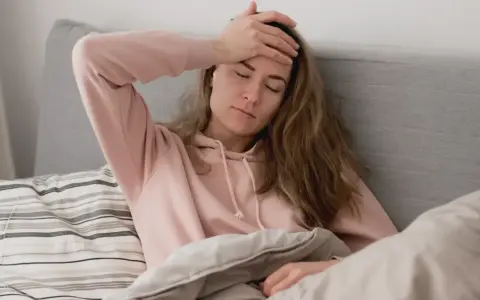 En kvinna med handen på pannan, insvept i täcken, upplever ångest direkt på morgonen.