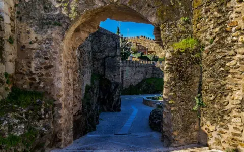 Un arco de piedra revela un camino empedrado y murallas, evocando la atmósfera de pueblos medievales cerca de Madrid.