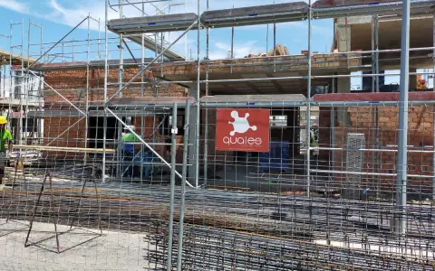 Obra en construcción con andamios y ladrillos. Se ve el logo de "qualee". ¿Cuánto se tarda en construir un edificio de 7 plantas?