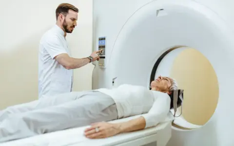 Pacjentka leży na stole do rezonansu magnetycznego, a technik obsługuje konsolę. Czy do rezonansu magnetycznego trzeba się rozebrać? Zazwyczaj tak, aby uniknąć zakłóceń.