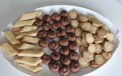 En vit oval bricka fylld med tre sorters hembakade småkakor: rombiska, chokladpraliner och runda med strössel. Perfekt för fika!