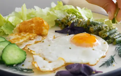 Un œuf au plat parfait, servi avec des haricots verts, des tranches de concombre, de la laitue et une touche de citron vert.
