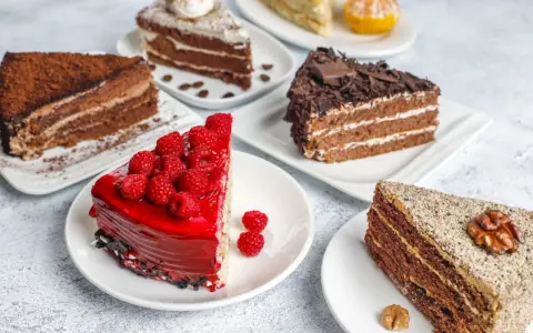 Variedad de pasteles en una mesa: uno de chocolate con cacao, otro con glaseado rojo y frambuesas, y uno con nueces. Una deliciosa carta de postres.