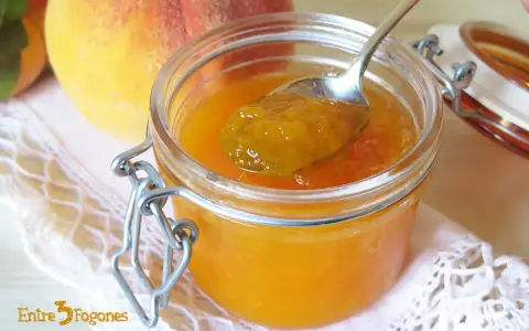 Cuchara con mermelada de melocotón casera, junto a melocotones frescos y un tarro de cristal.