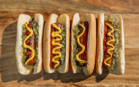 Cuatro hot dogs con mostaza, kétchup y cebolla picada sobre una tabla de madera.