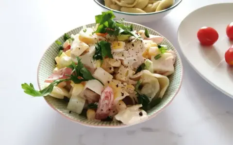 Pyszna sałatka z tortellini, jajka, kukurydzy i pomidorów, udekorowana natką pietruszki. Idealna na letnie dni.