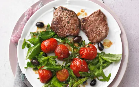 Zwei saftige Minutensteaks im Backofen zubereitet, serviert mit gerösteten Kirschtomaten, Rucola und schwarzen Oliven.