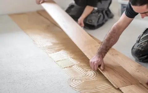 Handwerker verlegen sorgfältig Parkett auf Kleber. Die Holzbretter werden präzise nebeneinander gelegt, um ein schönes Ergebnis zu erzielen.