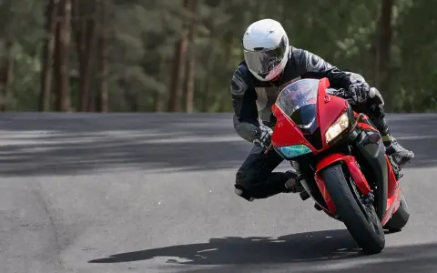 Motocyklista w białym kasku i czarnym kombinezonie pochyla się na czerwonym motocyklu podczas jazdy po drodze.