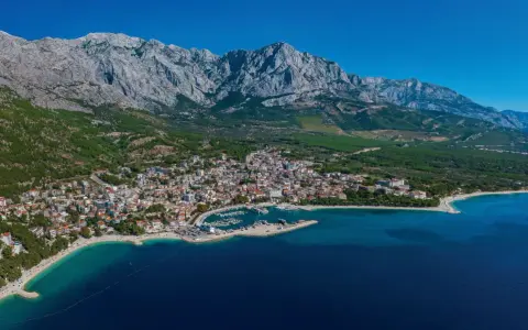 Widok na Baśkę Vodę z górami w tle. Atrakcje turystyczne obejmują plaże, port jachtowy i urokliwe miasteczko.