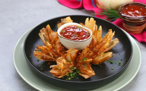 Eine knusprige, blühende Zwiebel, die wie eine Blume aussieht, mit einem Dip in der Mitte.