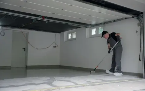 Mężczyzna maluje wałkiem podłogę w garażu, tworząc nowoczesną podłogę z żywicy. Jak zrobić taką podłogę?