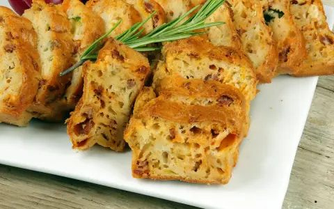 Tranches d'un cake salé au chorizo et poivron, garni de romarin, sur une assiette blanche.