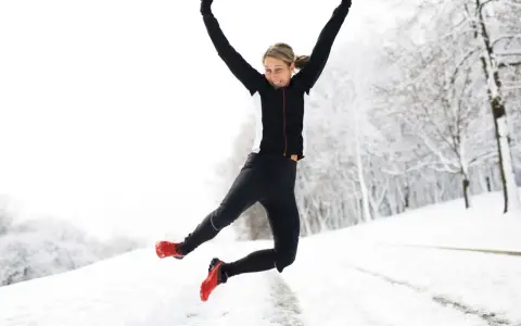Glad kvinna hoppar i snön, njuter av att springa i kyla. Vinterlandskap med träd.
