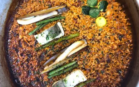 Deliciosa paella valenciana con arroz dorado, espárragos, pescado y navajas.