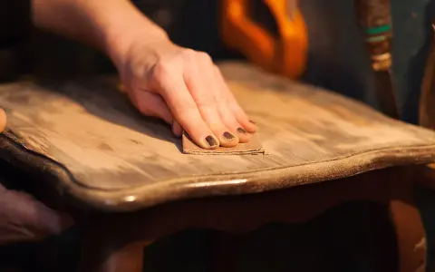 Main d'une personne ponçant un meuble en bois pour enlever la cire naturellement.