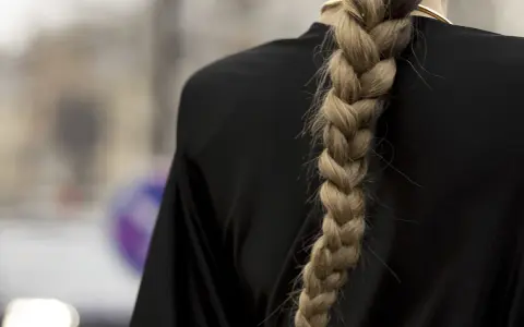 Gruby, blond warkocz opada na czarne ramię. To jedna z tych fryzur z warkoczem, które przyciągają wzrok.