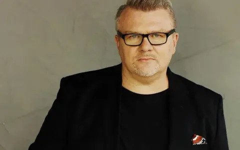 Rafał Michalak w czarnym garniturze i okularach, z charakterystyczną bródką. W kieszeni marynarki ozdobna poszetka.