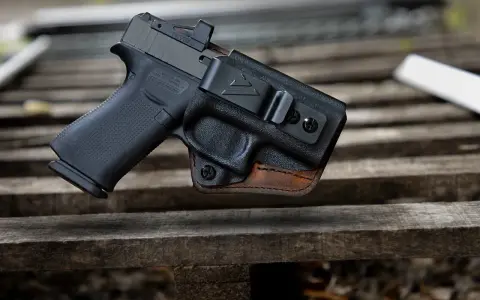 Pistolet w kaburze udowej z czarnego polimeru i brązowej skóry, z widocznym celownikiem optycznym.