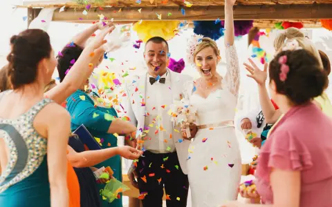 Glückliches Brautpaar im Konfettiregen, eine wunderschöne Tradition zur Hochzeit. Gäste werfen bunte Papierstreifen.