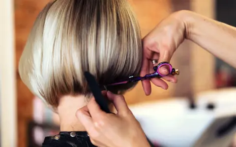 Fryzjerka modeluje cieniowany bob do ramion, używając nożyczek i grzebienia.
