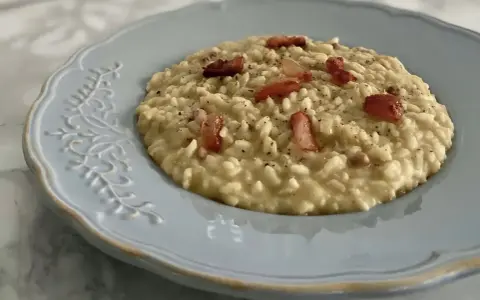 Un cremoso risotto con ceci e pancetta croccante, servito su un piatto azzurro decorato.
