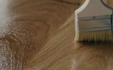 Brocha aplicando un acabado brillante sobre madera, mostrando diferentes tipos de barniz para madera.