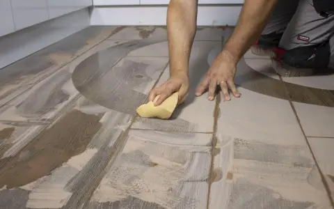 Man limpiando suelo porcelánico con una esponja. El suelo tiene un diseño de madera y un patrón curvo.
