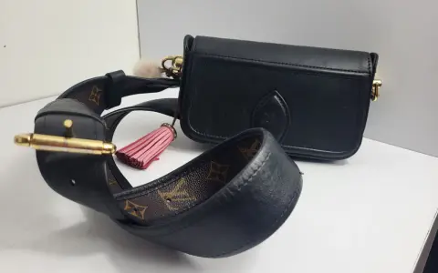 Elegancka, czarna louis vuitton torebka z ozdobnym, różowym pomponem i paskiem z monogramem.