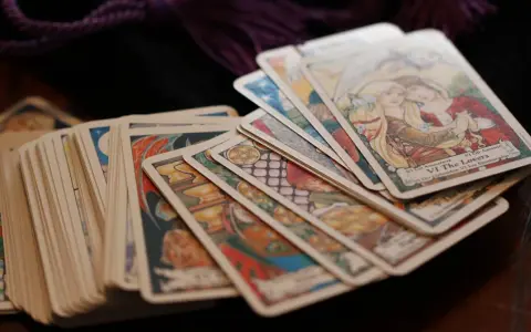 Karty tarota ułożone na drewnianym stole. Wśród nich widać kartę "Kochankowie". Sprawdź swój tarot tygodniowy skorpion.