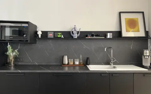 Encimera de cocina negra con vetas blancas, lista para cambiar. Microondas, fregadero y decoración moderna.