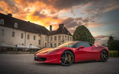 Czerwone Ferrari zaparkowane przed zabytkowym budynkiem podczas zachodu słońca.