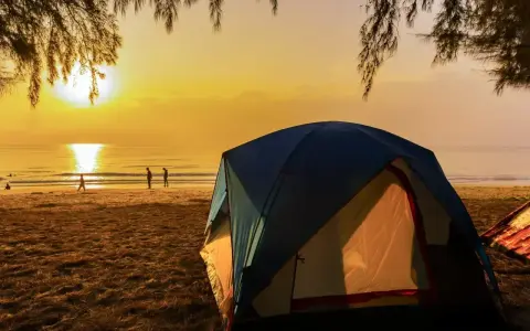 Kameralne pole namiotowe nad morzem. Słońce wschodzi nad spokojnym oceanem, rzucając złoty blask na plażę i namioty.
