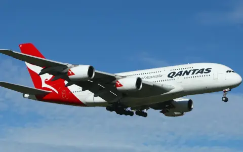 Gros avion Qantas, avec son logo rouge et blanc emblématique, en plein vol sous un ciel bleu.
