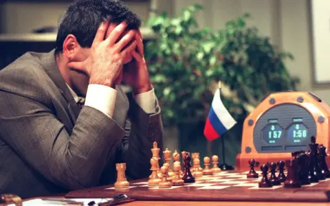 Garry Kasparov, le visage dans les mains, face à Deep Blue. L'horloge d'échecs affiche 1:57 et 1:56.